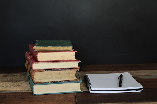 Pile of books beside white printer paper and black ballpoint pen